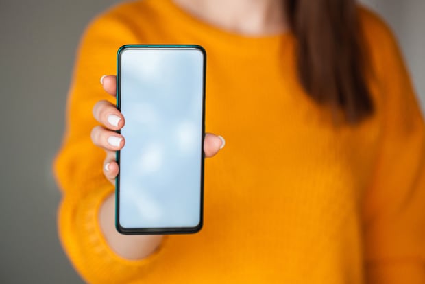 Woman hold mobile phone screen mockup in hands in orange sweater