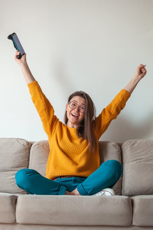 Woman gamer playing mobile phone online game, winner, holding in hands sitting on the sofa